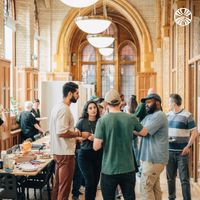 Group of diverse employees in discussion near a large, open hallway with arched ceilings.