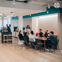 Open office space combining workstations, kitchen and dining area. Team members are sat around a communal dining table.