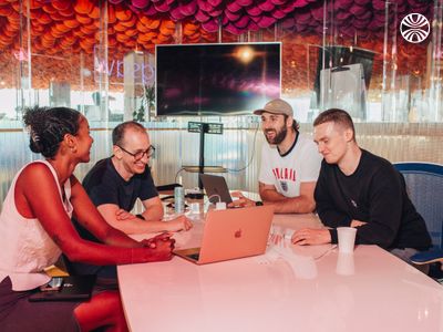 4 people, including a Black woman, collaborating around a laptop at a table.