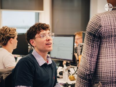 Colleagues collaborating in a kitchen area with casual conversation happening in the background.