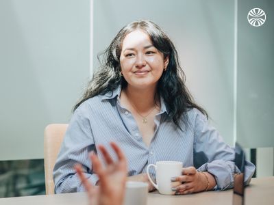 Team member participating in a discussion at a conference table, holding a coffee cup during the meeting.