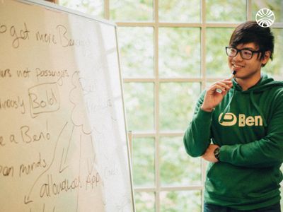 Man in green hoodie presenting at a whiteboard.