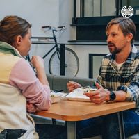 Two colleagues having a casual conversation at a table with a bicycle mounted on the wall behind them.
