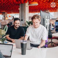 2 men smiling and collaborating at a desk in a shared office space.