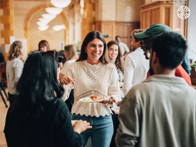 Diverse group of colleagues holding plates with snacks, engaged in discussion and smiling.