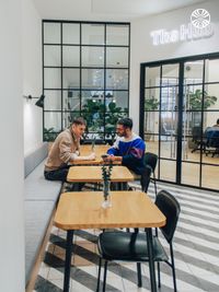 Two colleagues collaborating at a table in a bright breakout space with glass partitions and geometric floor patterns.