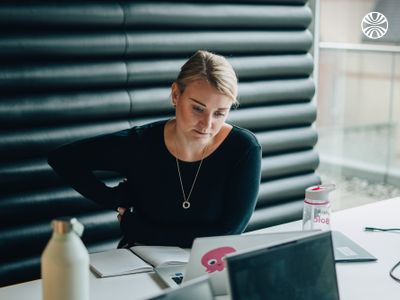 Person concentrating while reading documents at a desk, with laptop and water bottle nearby. Their laptop has a pink Octopus sticker on it.