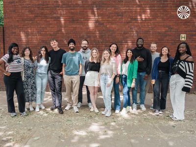 A diverse group of 14 colleagues stand together, posing for a photo on the street outside the office. 