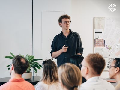 CEO Will Pearce leads the all hands, standing at the front of a minimalist room with plants.