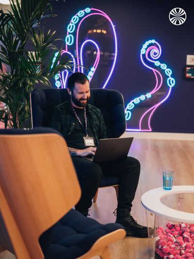 Professional working on a laptop in a lounge area, with decorative neon tentacle designs illuminating the wall behind.