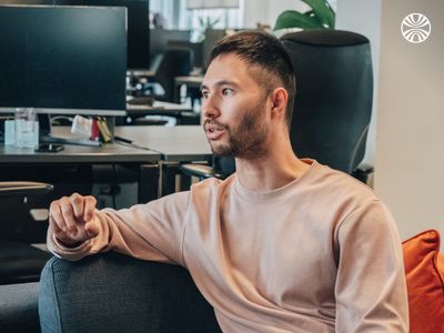 Colleague in a beige shirt, speaking and gesturing in a relaxed meeting setting.