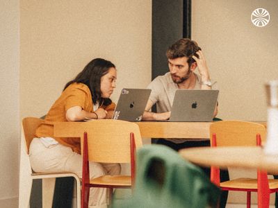 Two coworkers discussing over laptops at a table.