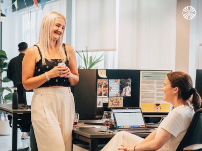 White woman standing and speaking to a seated colleague.