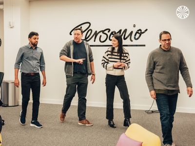 Four team members standing casually in an office space with "Personio" wall art, engaged in informal discussion.