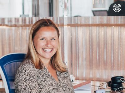 White woman smiling while sitting at a desk with a notebook.