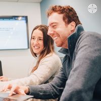 Two team members laugh while looking at a laptop during a meeting.